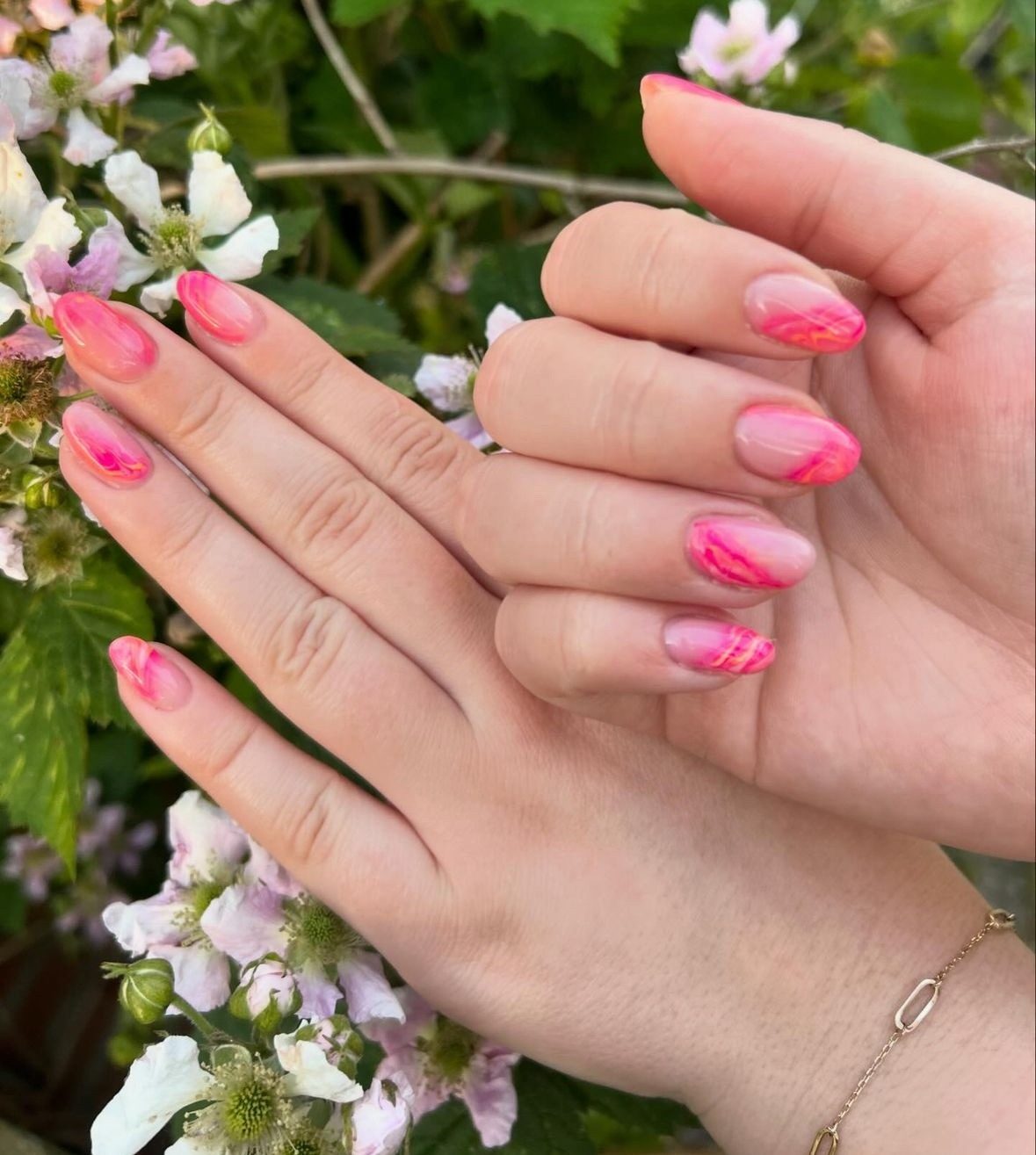 Roze gemarmerde nagels tussen witte braamstruikbloemen