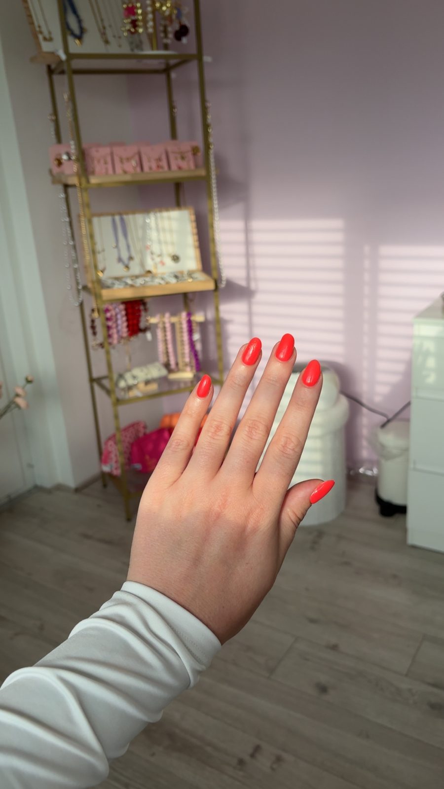 Hand met rode nagels in de salon, met een goudkleurig rek op de achtergrond