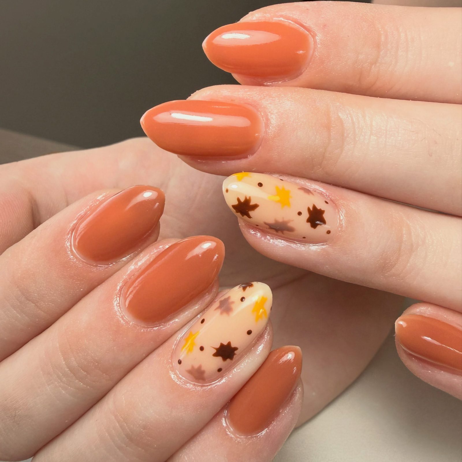 Oranje nagels met een herfstblad-design op twee accentnagels